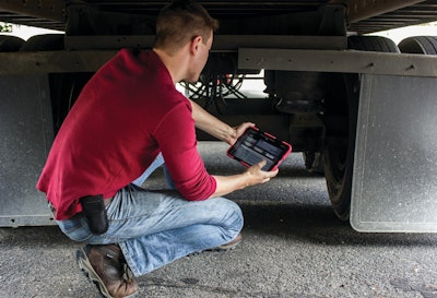 Man squatting down under semi-truck performing inspections with tablet