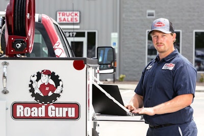 A man stands at the back of a mobile repair truck holding a laptop.