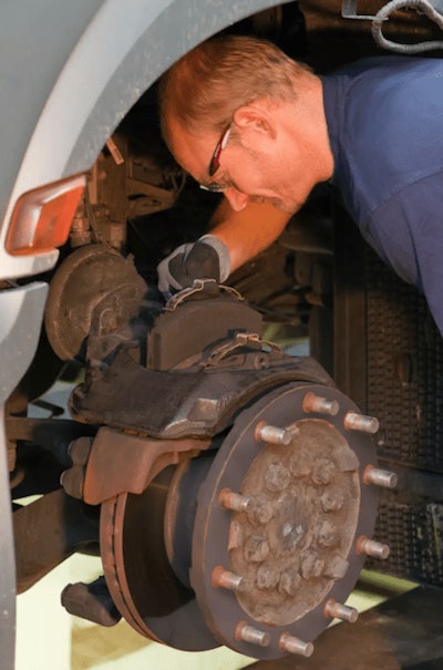 Technician measuring brake components under truck