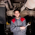 Younger technician poses under truck
