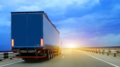 Truck with trailer driving down the road as the sun rises.