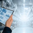 hands holding a tablet with graphs in the of a warehouse