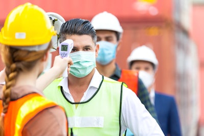 person checking the temperature of construction workers in a line