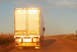 Tractor trailer driving down a rural road.