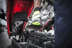 Truck technician holding wrench in front of a truck.
