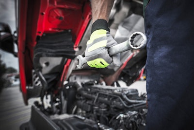 Truck technician holding wrench in front of a truck.