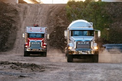 Two Mack Trucks driving down hill on gravel