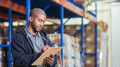 Man in warehouse writing on clipboard