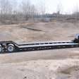 An unloaded gooseneck trailer on a work site.