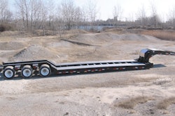 An unloaded gooseneck trailer on a work site.