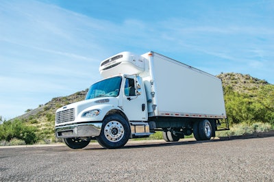 Refrigerated box truck parked on pavement in front of a hill.