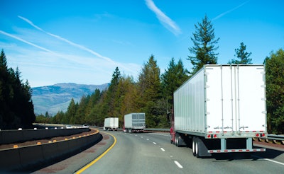 Three tractor-trailers going down the road into the mountains.