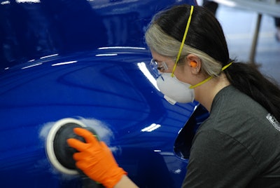 A woman works on the fender of a truck.