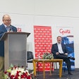 A man speaking at a podium with two other men seated behind.