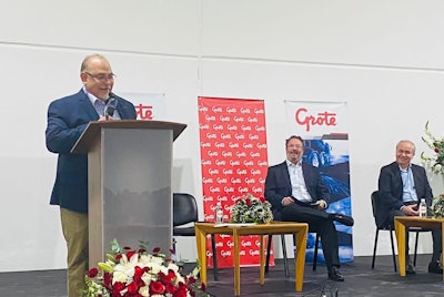 A man speaking at a podium with two other men seated behind.