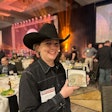A woman in a black shirt and black cowboy hat holds up a belt buckle.