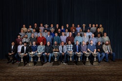 A large group of people in front of a curtain backdrop with trophies in front.