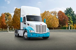 A white and blue Class 8 truck in front of trees.