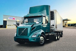 A green tractor-trailer in front of a dealership.