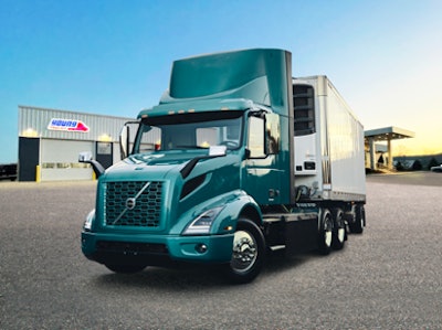 A green tractor-trailer in front of a dealership.