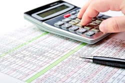 A hand poised over a calculator and spreadsheet.