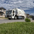 An electric garbage truck in front of a home.