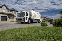 An electric garbage truck in front of a home.