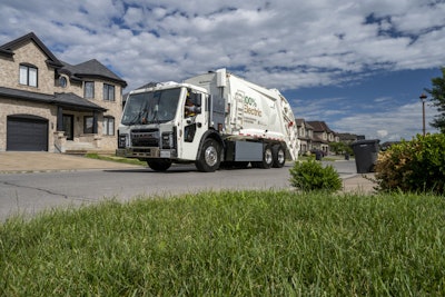 An electric garbage truck in front of a home.