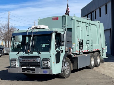 A mint green Mack LR Electric refuse truck at Bruckner Truck Sales in Commerce City, Colorado.