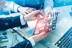 A graphic of hands holding a tablet with charts, graphs and other data.