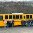 A group of people stand in front of an electric school bus.