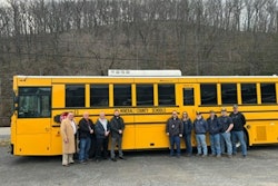 A group of people stand in front of an electric school bus.