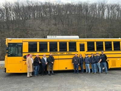 A group of people stand in front of an electric school bus.