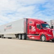 A red Kodiak autonomous truck pulling a white Forward trailer in a lot.
