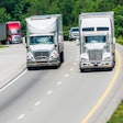 Trucks driving over a hill with trees in the background.