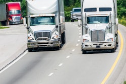 Trucks driving over a hill with trees in the background.