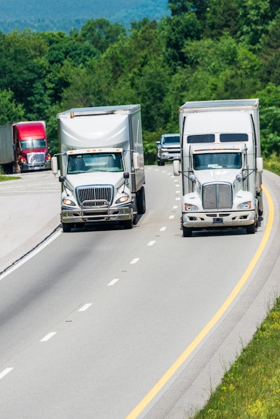 Trucks driving over a hill with trees in the background.