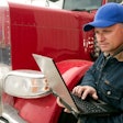Man standing next to a truck holding a laptop