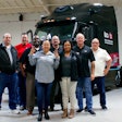 A group of people standing in front of a black Waabi autonomous truck.