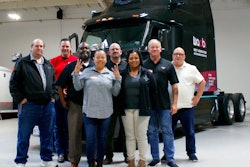 A group of people standing in front of a black Waabi autonomous truck.