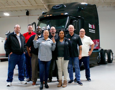 A group of people standing in front of a black Waabi autonomous truck.