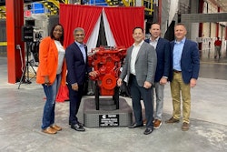 A group of people standing next to a red engine on a plinth.