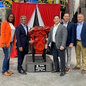 A group of people standing next to a red engine on a plinth.