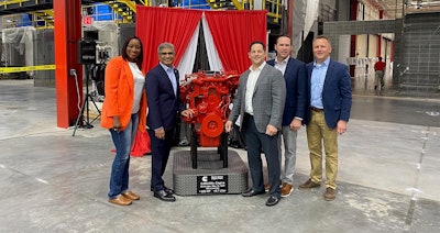 A group of people standing next to a red engine on a plinth.