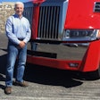 A man standing in front of a red Class 8 truck.