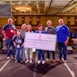 A group of people, some wearing St. Jude and some wearing FleetPride shirts, stand on stage in a crowded ballroom holding a giant check.