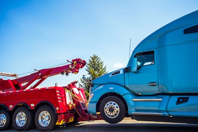 Red tow truck pulling a blue Class 8 tractor.