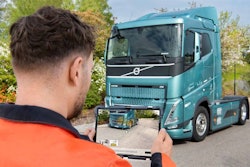 A man holding a tablet in front of a blue Volvo truck.