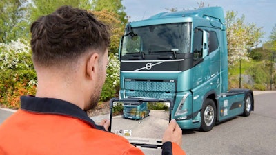 A man holding a tablet in front of a blue Volvo truck.