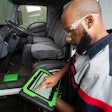 A man uses a green Bosch diagnostic tablet on a truck.